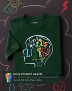 Folded LUUM's Every Emotion Counts t-shirt placed on chalkboard with doodles symbolizing emotions, creating a playful, expressive backdrop.Part of Threadmark Collection. Belief. Woven and Worn.