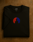 Front view of the LUUM's Samyak tee — black Supima cotton t-shirt with Buddha silhouette design in red and blue, symbolizing balance and focus. Part of Threadmark Collection. Belief. Woven and Worn.